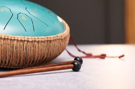 Steel tongue drum and mallets on light gray textured table indoors, closeup. Space for text
