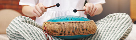 Woman playing steel tongue drum with mallets at home, closeup