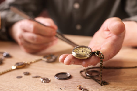 Senior man fixing mechanism of vintage wrist watch at wooden table indoors, closeup