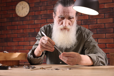 Senior man fixing mechanism of vintage wrist watch at wooden table indoors