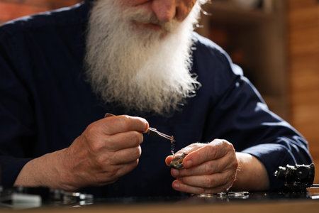 Senior man fixing mechanism of vintage wrist watch at table indoors, closeup