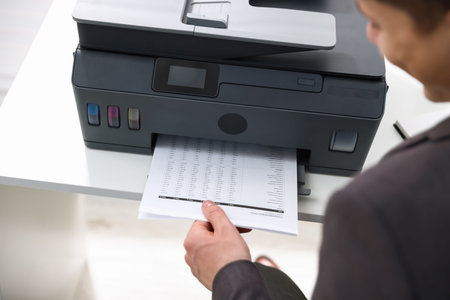 Man taking printed sheet of paper from printer at white desk indoors, closeup