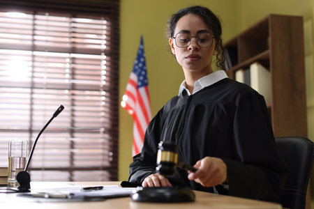 Judge striking gavel at wooden desk indoors