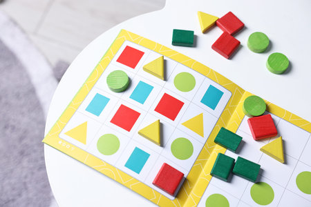 Open book and colorful pieces of geometrical sudoku for children on white table indoors, above view