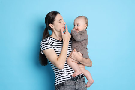 Mother with her cute baby on light blue background