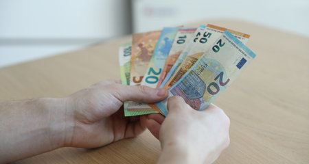 Man with euro banknotes at wooden table, closeup