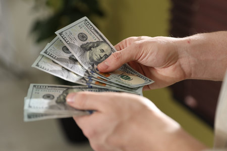 Man counting dollar banknotes indoors, closeup view