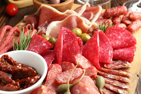 Charcuterie board with different cured meat, sausages and olives on wooden table, closeup