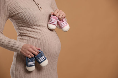 Pregnant woman with baby shoes on beige background, closeup. Space for textの写真素材