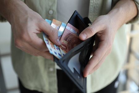 Man putting euro banknotes into wallet indoors, closeup