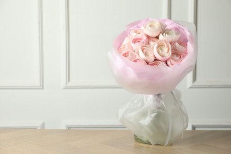 Bouquet of beautiful ranunculus flowers on wooden table near white wall indoors, space for text