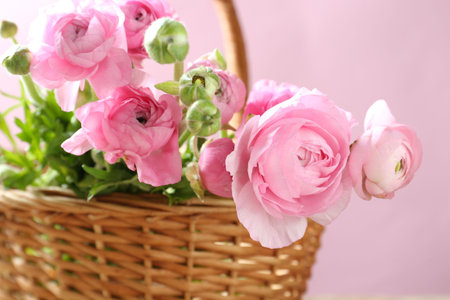 Beautiful flowers in wicker basket on pink background, closeup