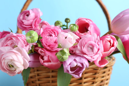 Beautiful flowers in wicker basket on light blue background, closeup