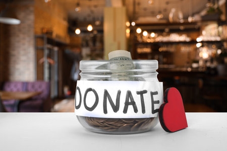 Donation jar with money and red wooden heart on table in cafeの写真素材