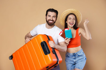 Happy couple with suitcase, passports and tickets on beige background