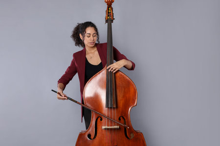 Woman playing double bass on gray background