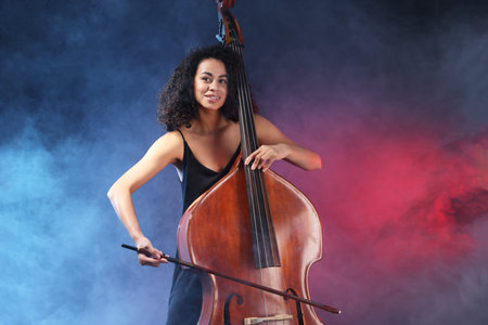 Woman playing double bass on dark background with smoke