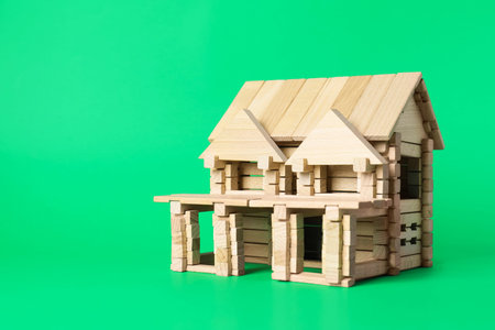 House made of wooden blocks on green background. Space for text