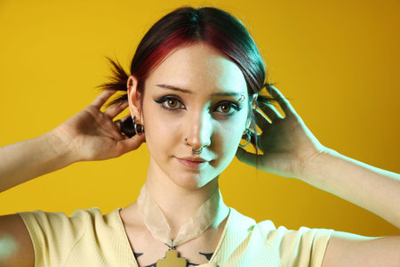 Portrait of beautiful young woman with piercings in color light on yellow background