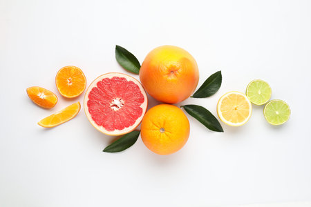 Different fresh citrus fruits and green leaves on white background, flat lay