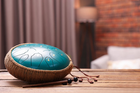 Steel tongue drum and mallets on wooden table indoors, closeup. Space for text