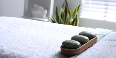 Stones on massage bed in spa center, closeup. Space for text