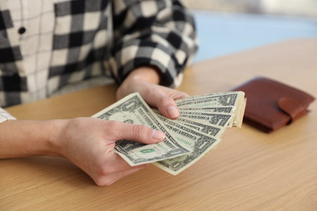 Woman counting dollar banknotes at wooden table, closeup