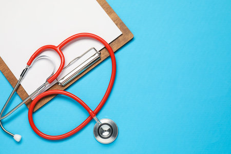 Stethoscope and clipboard on light blue background, top view. Space for text