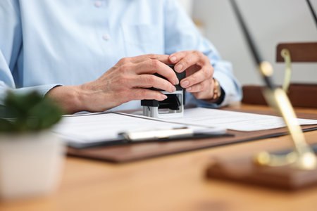 Notary stamping document at desk in office, closeup