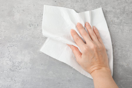 Woman wiping gray textured surface with paper towel, top view