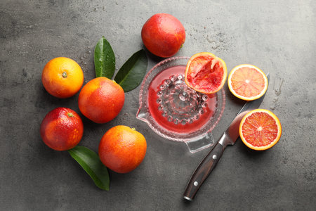 Ripe Sicilian oranges, squeezer, knife and green leaves on gray table, flat lay