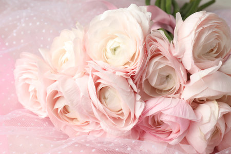 Many beautiful ranunculus flowers and tulle cloth on pink background, closeup
