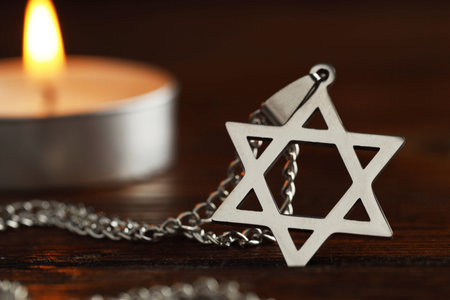 Holocaust Remembrance Day. Pendant in shape of Star of David and burning candle on wooden table...