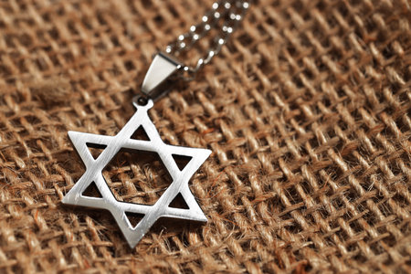 Holocaust Remembrance Day. Pendant in shape of Star of David on burlap cloth, closeup. Space for...