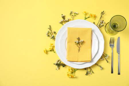 Beautiful table setting with floral decor on yellow background, flat lay. Space for text