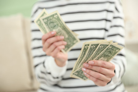 Woman counting dollar banknotes indoors, closeup view