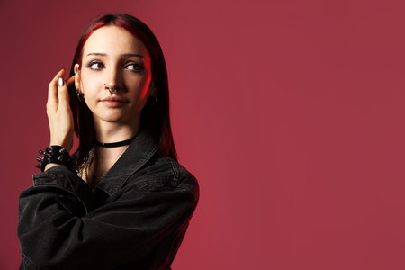Beautiful young woman with piercings and jacket in red light on pink background. Space for text