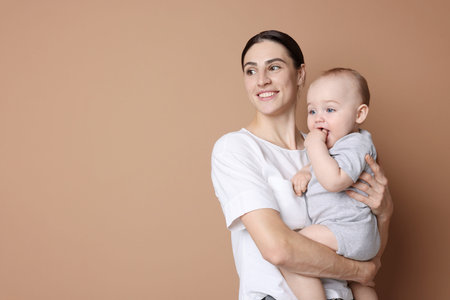 Happy mother with her cute baby on beige background, space for text