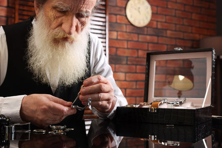 Senior man fixing mechanism of vintage wrist watch at black mirror table indoors