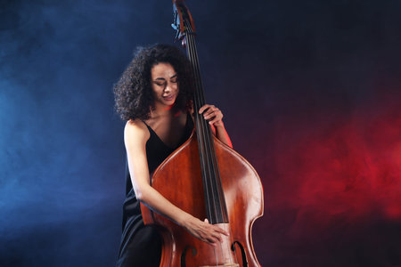 Woman playing double bass on dark background in neon lights with smoke