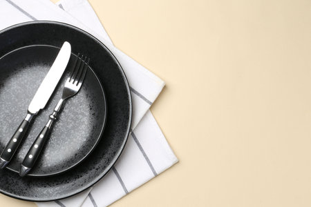 Stylish setting with cutlery and napkin on beige table, top view. Space for text