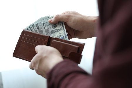 Man putting dollar banknotes into wallet against blurred background, closeup