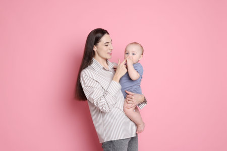 Happy mother with her cute baby on pink background
