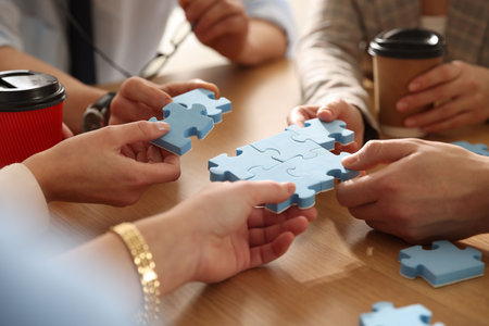 Team building. Group of businesspeople holding puzzle pieces together at wooden table, closeup