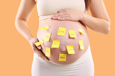 Pregnant woman with notes with different names on her belly against orange background, closeupの写真素材