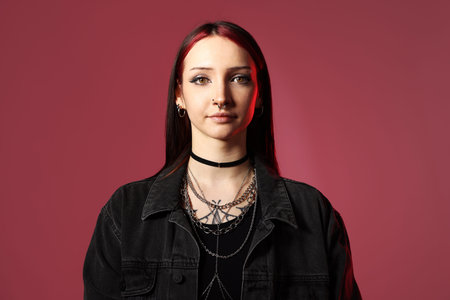 Portrait of beautiful young woman with piercings and stylish accessories in red light on pink...