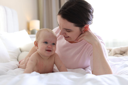 Mother and her cute baby on bed at home