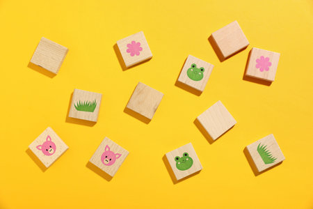 Wooden tiles with pictures of children's game and blank ones on yellow background, flat lay