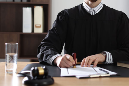 Portrait of smiling judge in glasses stamping document at table in office