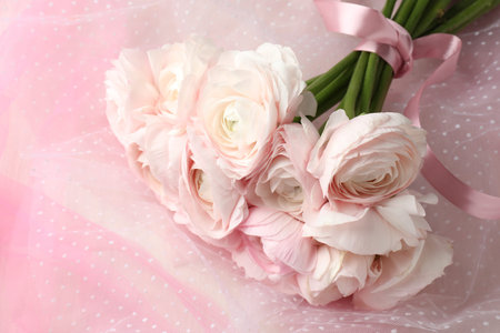 Bouquet of beautiful ranunculus flowers and tulle cloth on table, top view
